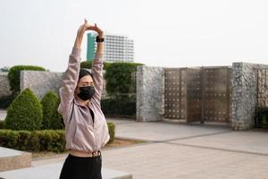 selectief focus Bij gezicht van jong mooi Aziatisch Dames vervelend chirurgisch gezicht masker terwijl uitrekken warm omhoog voordat oefening of rennen Bij de park in de ochtend. nieuw normaal levensstijl. foto