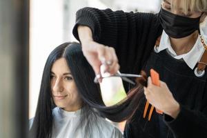 Kaukasisch Dames met haar- elegant terwijl Doen haar- besnoeiing en vervelend chirurgisch gezicht masker terwijl styling haar- voor cliënt. professioneel bezigheid, schoonheid en mode onderhoud nieuw normaal foto