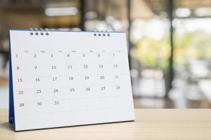 wit papier bureau kalender Aan hout tafel met wazig bokeh achtergrond afspraak en bedrijf vergadering concept foto