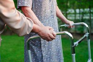 verzorger helpt aziatische oudere vrouw handicap patiënt lopen met rollator in verpleegziekenhuis, medisch concept. foto