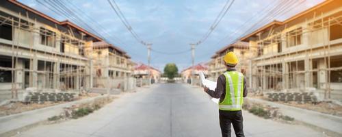 jong professioneel ingenieur in beschermend helm en blauwdrukken papier Bij de huis gebouw bouw plaats foto