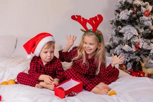 twee gelukkig kinderen in pyjama voor Kerstmis zijn sorteren presenteert en spelen met Kerstmis speelgoed. hoog kwaliteit foto