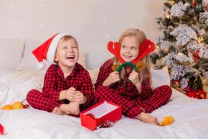 twee gelukkig kinderen in pyjama voor Kerstmis zijn sorteren presenteert en spelen met Kerstmis speelgoed. hoog kwaliteit foto