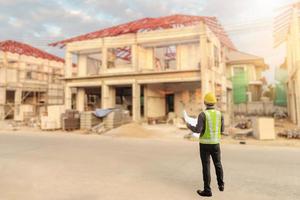 jong professioneel ingenieur in beschermend helm en blauwdrukken papier Bij de huis gebouw bouw plaats foto