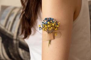 blauwe en gele bloem onder de patch op de hand van een vrouw. het concept van vaccinatie en behandeling in oekraïne foto