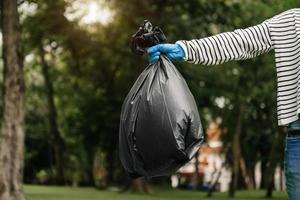 hand- Holding vuilnis zwart zak zetten in naar uitschot naar schoon. opruimen, vervuiling, ecologie en plastic concept. Bij park foto