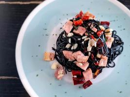 Italiaans smakelijk voedsel. zwart inktvis inkt spaghetti pasta met ham spek knoflook en droog chili versierd Aan pastel kleur bord foto