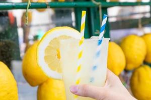 Kaukasische hand met gezonde verse limonade tijdens de zomer - citroenenachtergrond foto