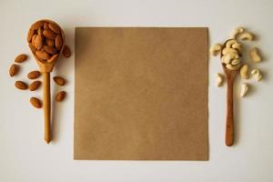 twee houten lepels met amandel en cachou noten Aan de wit achtergrond met papier. foto