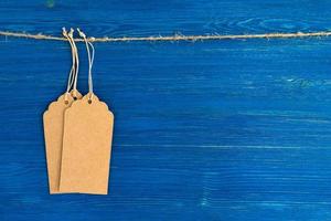 drie bruin blanco papier prijs tags of etiketten reeks hangende Aan een touw Aan de blauw houten achtergrond. foto