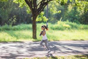 gelukkig kind meisje rennen in de park in zomer in natuur. warm zonlicht gloed. Aziatisch weinig is rennen in een park. buitenshuis sport- en fitheid, oefening en wedstrijd aan het leren voor kind ontwikkeling. foto