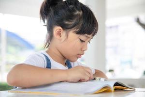 Aziatisch weinig meisje lezing de boeken Aan de bureau met een vergroten glas foto