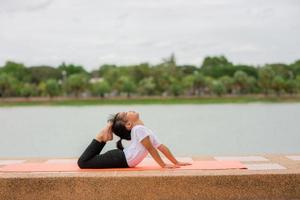 weinig schattig Aziatisch meisje beoefenen yoga houding Aan een mat in park, gezond en oefening concept foto