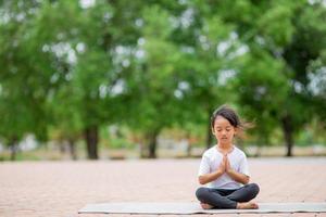 weinig schattig Aziatisch meisje beoefenen yoga houding Aan een mat in park, gezond en oefening concept foto