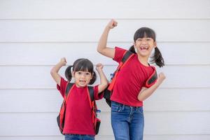 vrolijk glimlachen weinig meisje met groot rugzak jumping en hebben pret tegen de wit muur. op zoek Bij de camera. school- concept. terug naar school- foto