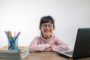 Aziatisch meisje zittend en aan het studeren Bij huis Aan een laptop naar studie van huis gedurende covid-19 pandemisch lockdown. online opleiding, thuisonderwijs foto