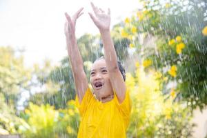 gelukkig Aziatisch weinig kind meisje hebben pret naar Speel met de regen in de zonlicht foto