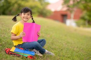 schattig klein meisje leesboek buiten op gras foto