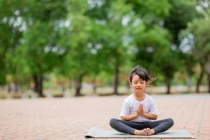 weinig schattig Aziatisch meisje beoefenen yoga houding Aan een mat in park, gezond en oefening concept foto