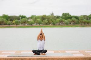 weinig schattig Aziatisch meisje beoefenen yoga houding Aan een mat in park, gezond en oefening concept foto