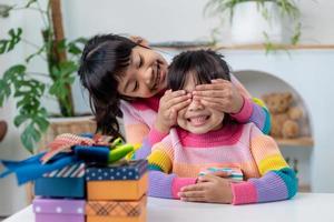 weinig meisje maken Cadeau naar weinig gelukkig kind meisje Holding geschenk doos, sluitend ogen van schattig glimlachen opgewonden met verjaardag verrassing van haar zus foto