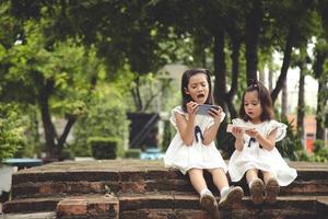 concept kinderen en gadgets. twee weinig meisjes broers en zussen zussen kijken Bij de telefoon. ze houden een smartphone kijk maar videos, leren, Speel spellen, spreken online. internet voor kinderen. foto