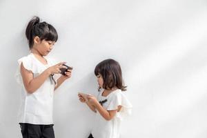 broer of zus meisjes aan het kijken hun smartphones Aan wit achtergrond. sociaal concept over nieuw technologie mensen verslaving foto