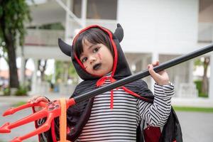 Aziatisch kind meisje in demon kostuum Holding zwart en rood drietand, gelukkig halloween concept foto