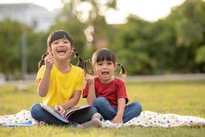 twee mooi weinig meisjes lezing boeken in de tuin , zittend Aan gras. de concept van onderwijs en vriendschap. foto