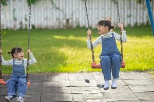 twee schattig weinig zussen hebben pret Aan een schommel samen in een mooi zomer tuin Aan een warm en zonnig dag buitenshuis. actief zomer vrije tijd voor kinderen. foto