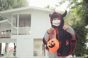 Aziatisch weinig meisje in een halloween kostuum in een medisch masker . halloween met veiligheid maatregelen van covid-19 foto