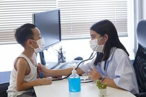 een Aziatisch vrouw dokter vervelend een chirurgisch masker is gieten alcohol gel Aan de patiënten hand. foto