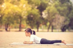 weinig schattig Aziatisch meisje beoefenen yoga houding Aan een mat in park, gezond en oefening concept foto
