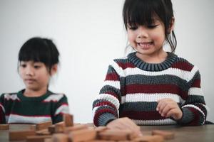 vrolijk Aziatisch meisje spelen met houten gebouw blokken. hebben pret en aan het leren creativiteit. slim kind concept. foto