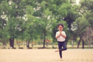 weinig schattig Aziatisch meisje beoefenen yoga houding Aan een mat in park, gezond en oefening concept foto