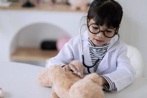 Aziatisch meisje spelen met haar geduldig pluche beer in een dokter spel, gebruik makend van een stethoscoop. kinderen willen naar worden een kinderarts dokter foto