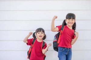 vrolijk glimlachen weinig meisje met groot rugzak jumping en hebben pret tegen de wit muur. op zoek Bij de camera. school- concept. terug naar school- foto