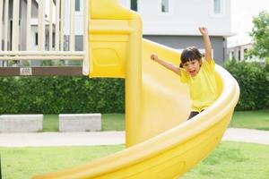 kind spelen Aan buitenshuis speelplaats. kinderen Speel Aan school- of kleuterschool tuin. actief kind Aan kleurrijk glijbaan en schommel. gezond zomer werkzaamheid voor kinderen. foto