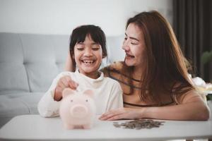 moeder en dochter zetten munten in varkentje bank. familie begroting en spaargeld concept. junior spaargeld account concept foto