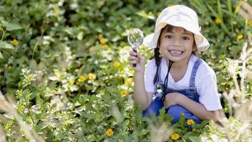 Aziatisch weinig meisje is op zoek Bij boom bladeren door vergrootglas, buitenshuis schieten foto