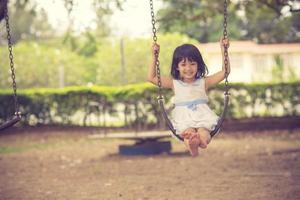 weinig meisje swinging Aan schommel Bij park foto