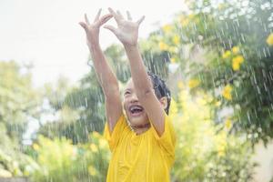 gelukkig Aziatisch weinig kind meisje hebben pret naar Speel met de regen in de zonlicht foto