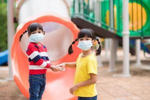 nieuw normaal levensstijl, sociaal afstand nemen concept. gelukkig kinderen vervelend gezicht masker hebben pret Aan Bij speelplaats beschermen coronavirus covid19, foto