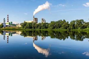 pijpen van houtbewerking onderneming fabriek zagerij met mooi reflectie in blauw water van rivier. lucht verontreiniging concept. industrieel landschap milieu verontreiniging verspilling van thermisch macht fabriek foto