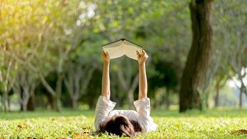 een mooi Aziatisch vrouw aan het liegen en lezing een boek in de park.concept van aan het studeren, aan het leren en interessant van de literatuur. foto