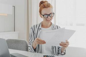 gelukkige glimlachende blanke vrouw die goed nieuws leest in financiële documenten terwijl ze het gezinsbudget beheert foto