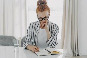 roodharige vrouw in gestreept shirt maakt aantekeningen en schrijft informatie op in notitieboekje foto