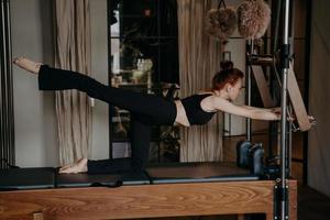 jonge gember atletische vrouw oefenen op pilates hervormer in studio foto