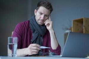 ongezond uitziende mannelijke freelancer die zich onwel en koud voelt, warme gebreide sjaal om de nek draagt foto