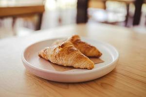 twee smakelijk croissants Aan een bord zijn geplaatst Aan een houten tafel in de cafe. foto